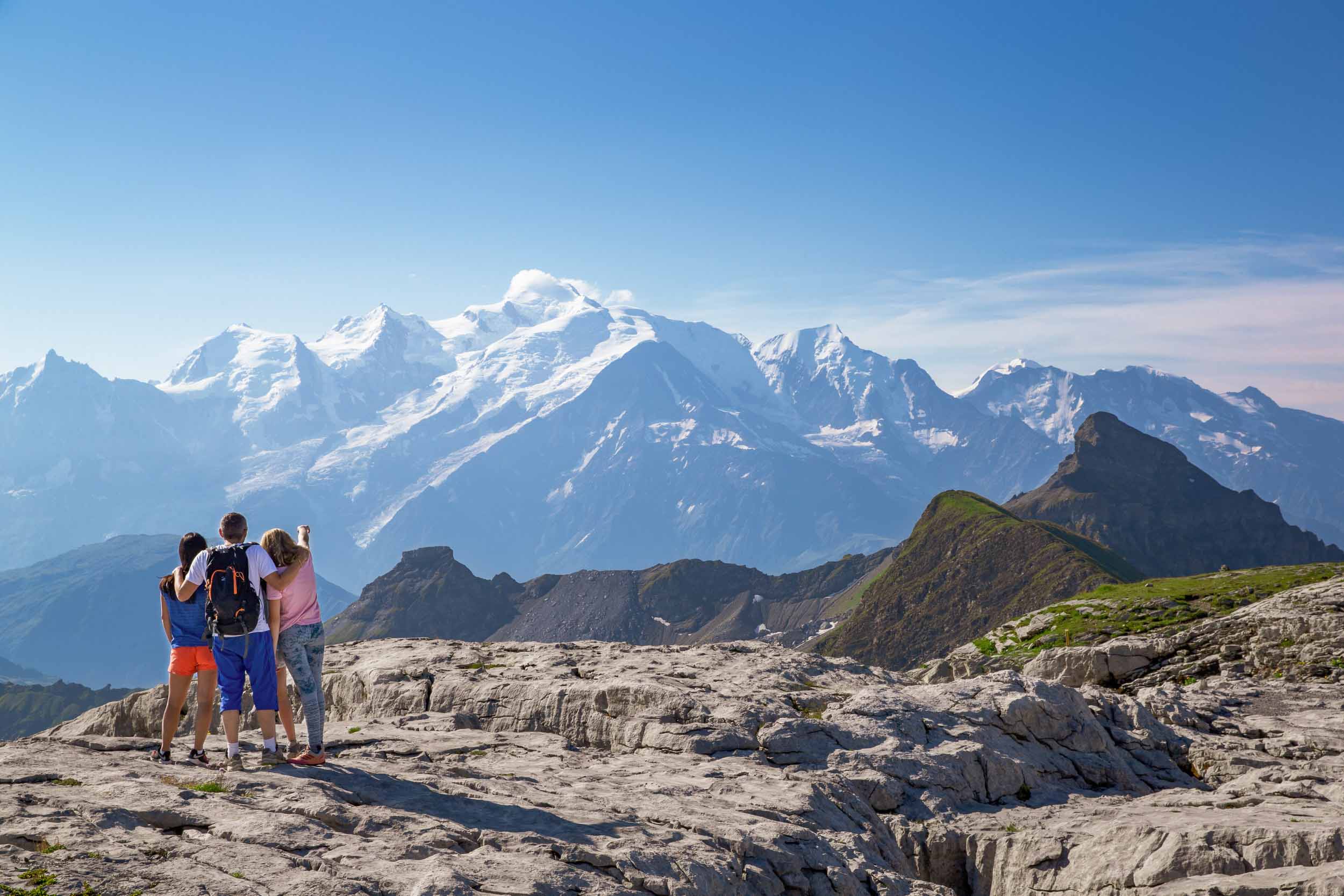 Randonneurs au sommet des Grandes Platières sur le Désert de Platé à Flaine, admirant les montagnes enneigées du Mont Blanc sous un ciel bleu clair.