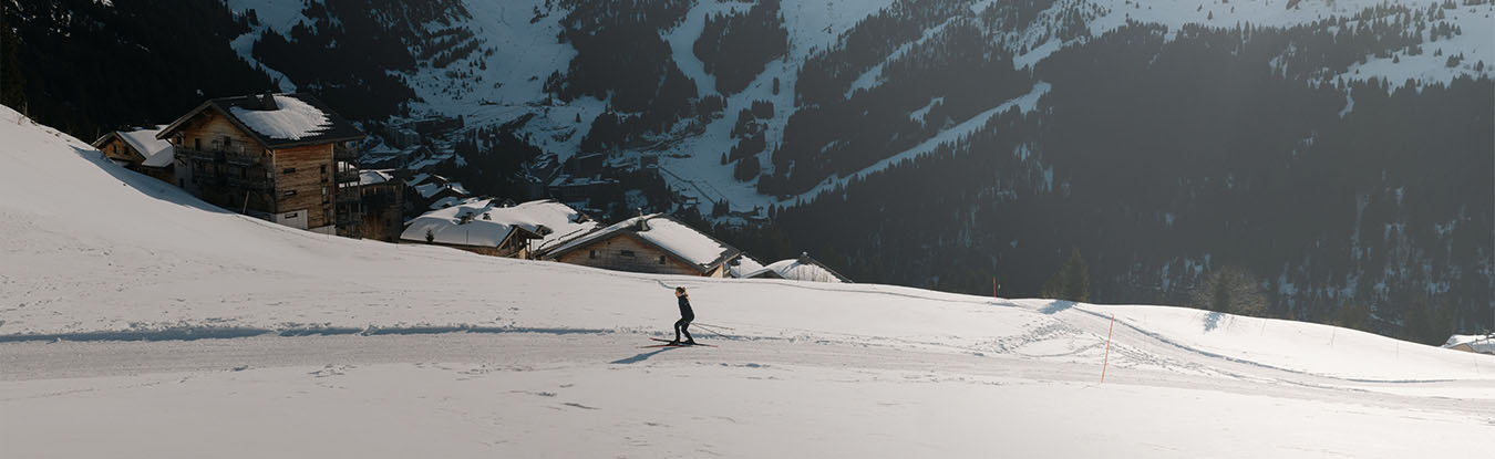 Une séance de ski de fond au Col de Pierre Carrée, à Flaine. Le cliché capture une skieuse en plein effort sur une piste enneigée, bordée de chalets typiques avec, en arrière-plan, le relief escarpé des montagnes de Haute-Savoie.